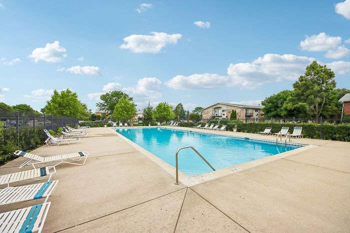 Inviting outdoor pool area surrounded by lush greenery and comfortable lounge chairs under a bright blue sky.