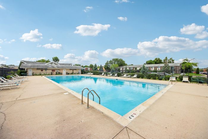 Inviting outdoor pool area featuring clear blue water, sun loungers, and a serene backdrop of lush greenery under a bright, blue sky.