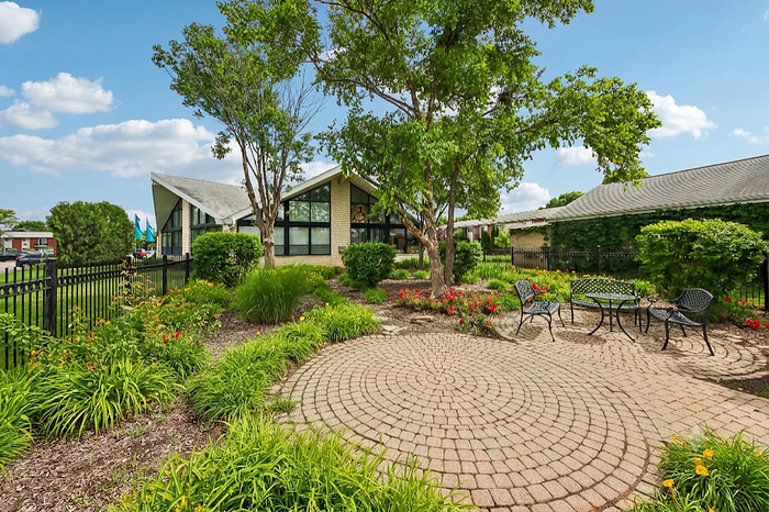 Charming landscaped garden with brick patio, surrounded by lush greenery and outdoor seating, perfect for relaxation and entertainment.