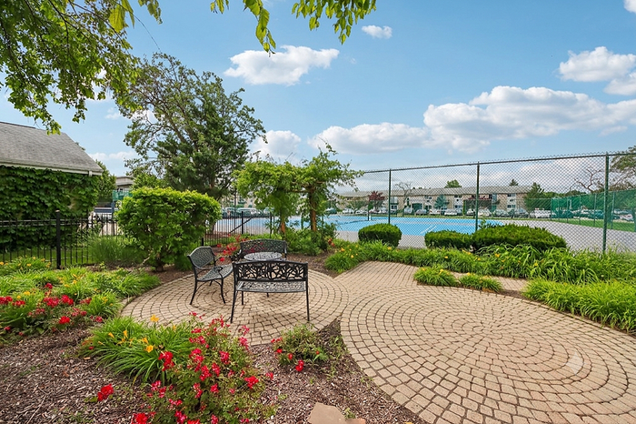 Charming outdoor patio with elegant wrought iron seating, vibrant flower beds, and lush greenery, adjacent to a spacious tennis court.