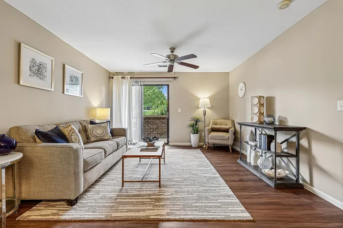 Inviting living room featuring a cozy sofa, elegant decor, and a sleek coffee table, bathed in natural light from a patio door overlooking greenery.