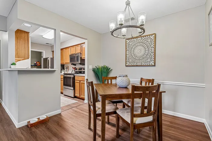 Elegant dining area with a wooden table set beneath a stylish chandelier, adjacent to a modern kitchen with stainless steel appliances.