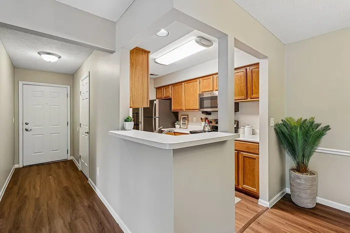 Inviting and contemporary apartment entry featuring warm wood flooring, a modern kitchen with stainless steel appliances, and a stylish breakfast bar adorned with greenery.