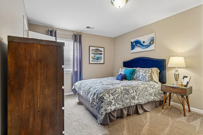 Elegant bedroom with a cozy bed, artistic wall decor, and rich wooden furniture, bathed in natural light from the window.