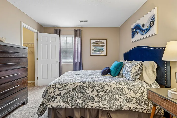 Inviting bedroom featuring a plush bed with elegant patterned bedding, complemented by a rich blue headboard and stylish wall art.