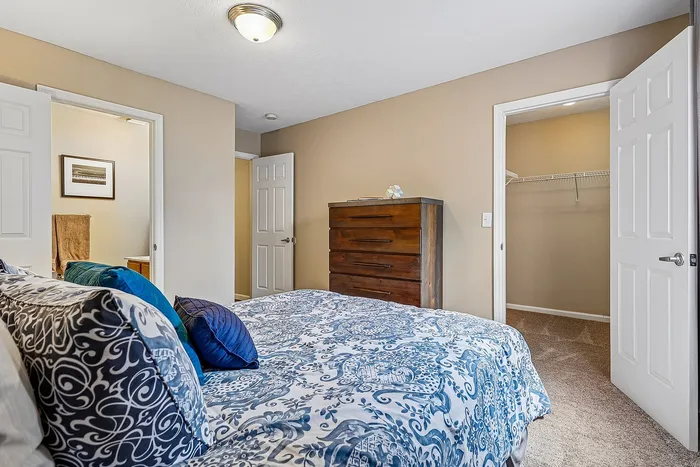 Inviting bedroom with elegant decor, featuring a plush bed with patterned bedding, a chest of drawers, and access to a spacious walk-in closet and ensuite bathroom.