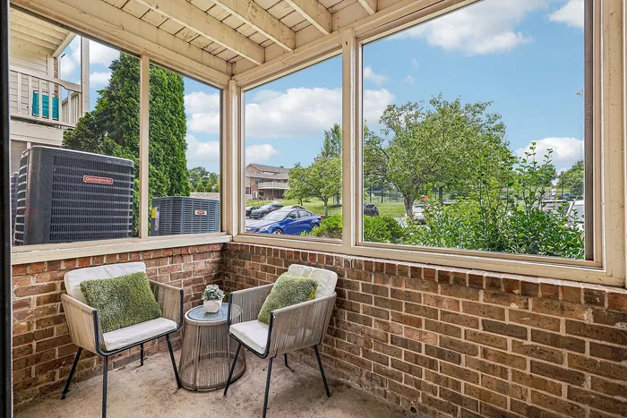 Charming enclosed patio with cozy seating and lush views, ideal for relaxing in a serene apartment community.