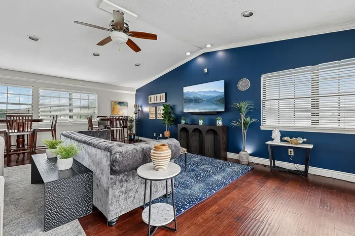 Elegant open living room with plush velvet sofa, dark hardwood flooring, and a striking blue accent wall featuring modern decor and large windows for natural light.