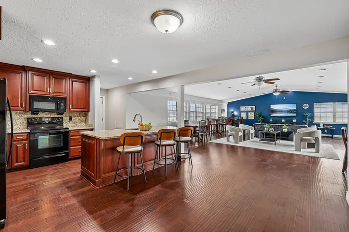 Elegant open-concept kitchen and living area featuring rich wood cabinetry, a stylish island with seating, and a chic blue accent wall.