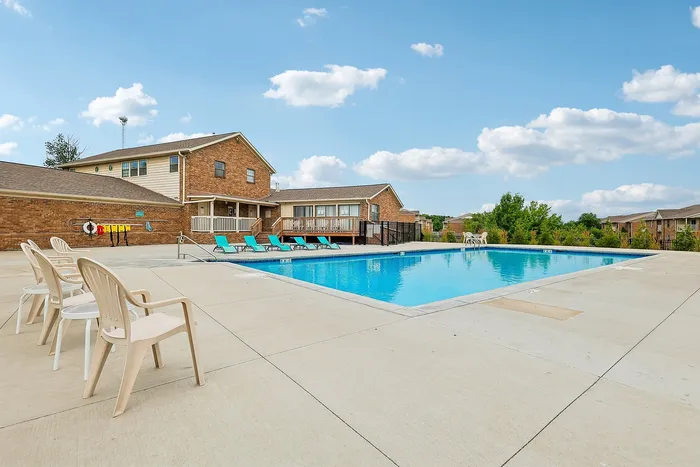 Inviting residential swimming pool area with bright lounge chairs and clear blue skies, perfect for relaxation in a beautiful community setting.