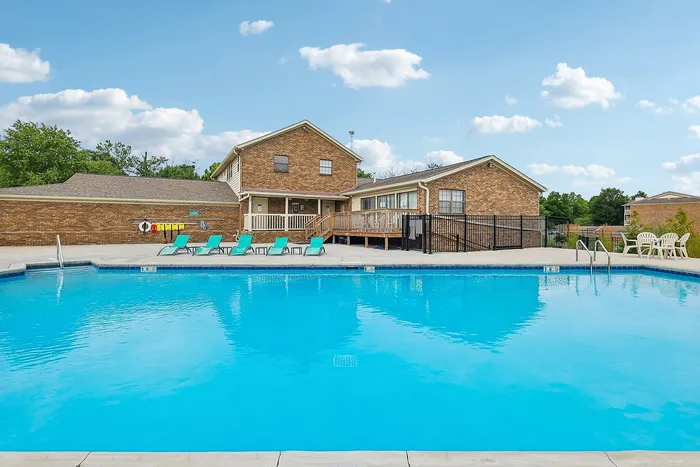 Inviting residential pool area with sun loungers, adjacent to a charming brick building under a bright blue sky.