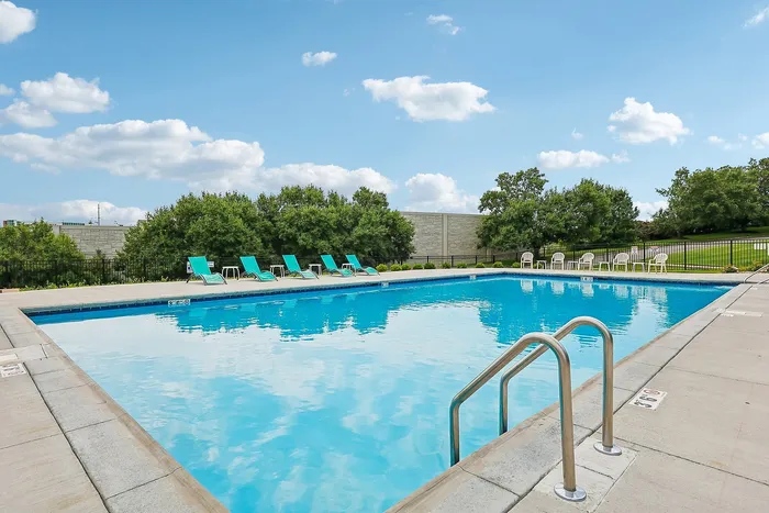 Inviting swimming pool with turquoise lounge chairs set against a backdrop of lush greenery and a clear blue sky.