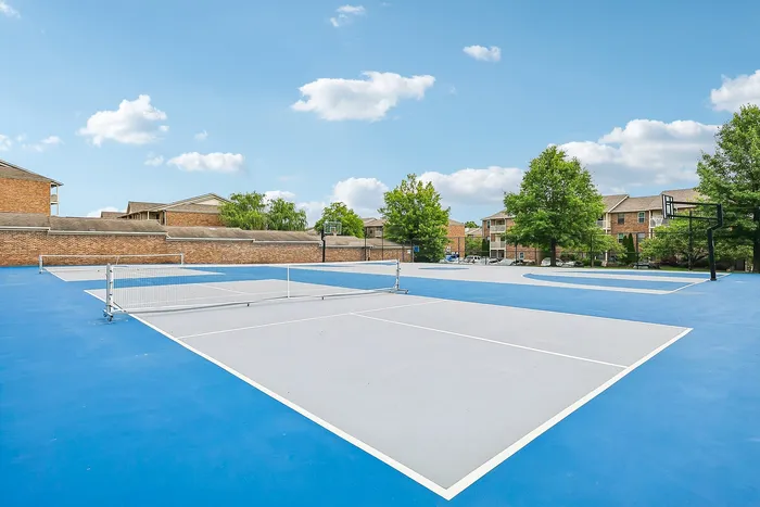 Modern recreational area with spacious tennis and basketball courts surrounded by lush greenery and charming brick buildings.