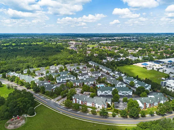 Aerial view of a vibrant apartment complex surrounded by lush greenery, showcasing modern living amidst serene landscapes.