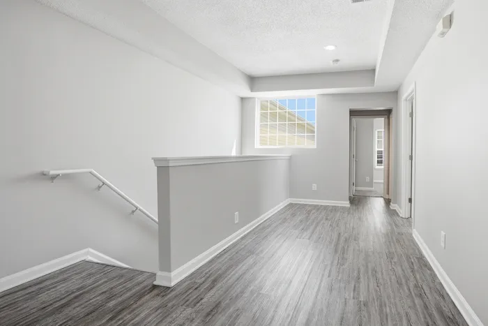 Bright and modern hallway with sleek hardwood flooring, large window, and minimalistic design leading to a cozy room.