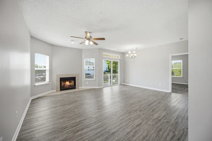Charming living room with elegant wooden flooring, cozy fireplace, ceiling fan, and abundant natural light through large windows.