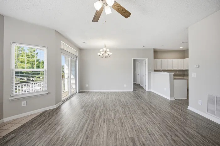 Bright and airy living space with elegant wood flooring, a modern chandelier, and a seamless flow into a pristine kitchen.