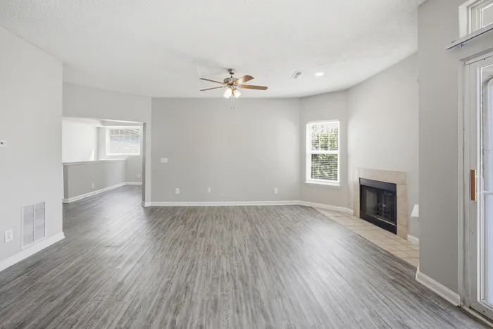 Spacious living room featuring elegant wood flooring, modern ceiling fan, and a cozy fireplace with natural light streaming in from large windows.