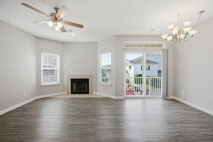 Bright and airy living room boasting a modern chandelier, cozy fireplace, and sleek hardwood floors with ample natural light from large windows.