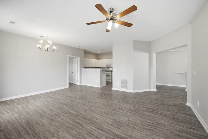 Bright open-floor living space featuring elegant wood laminate flooring, modern ceiling fan, and a stylish kitchen with white cabinetry.