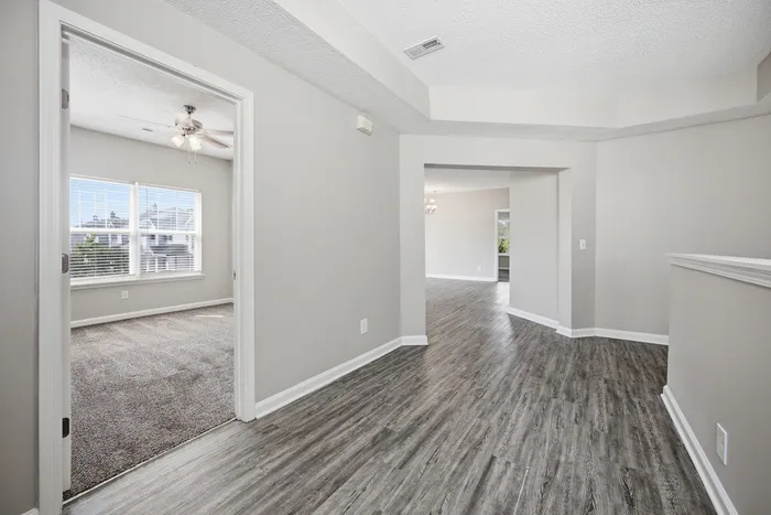 Bright and modern apartment interior featuring sleek laminate flooring, a cozy carpeted room, and large sunlit windows.