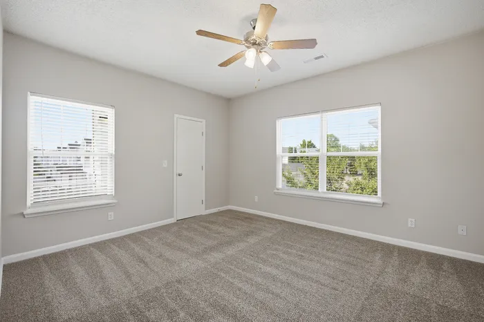 Bright and airy bedroom with plush carpeting, large windows offering scenic views, and a modern ceiling fan.