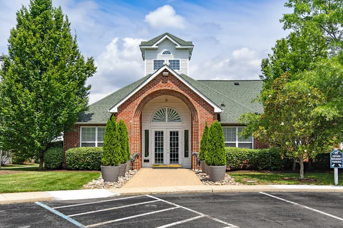 Charming brick building with a welcoming arched entrance, surrounded by lush greenery and parking spaces for future residents.