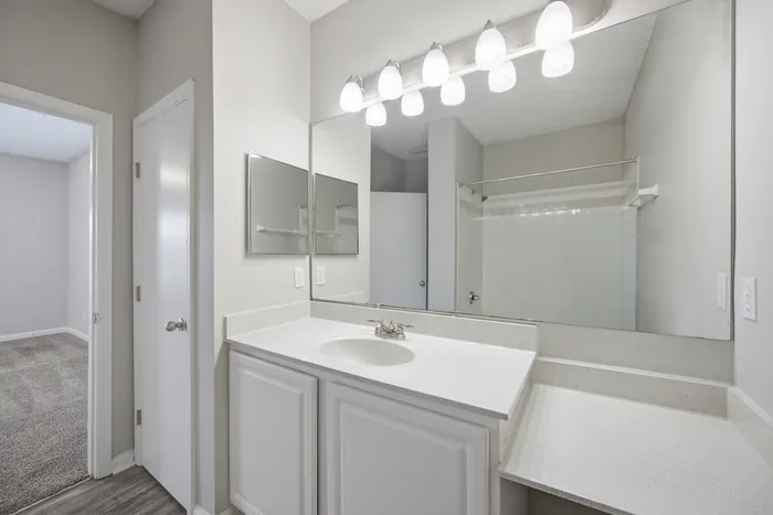Bright and elegant bathroom with a large mirror, modern lighting, and a sleek white vanity.