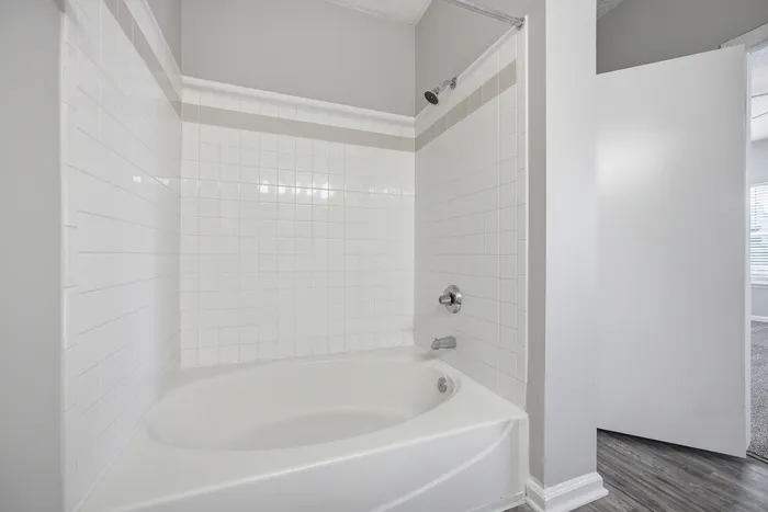 Modern bathroom featuring a pristine tiled bathtub and shower with sleek fixtures, offering a refreshing and clean ambiance.