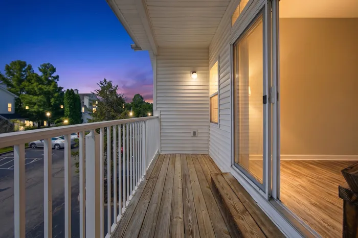Inviting balcony view at sunset with wooden deck, white railing, and warm interior glow through sliding glass doors.