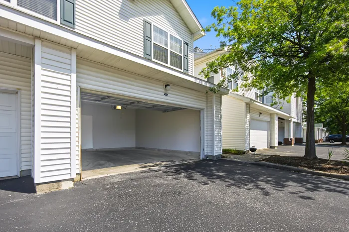 Charming townhouse with a spacious two-car garage and modern siding, surrounded by lush greenery in a quiet neighborhood.