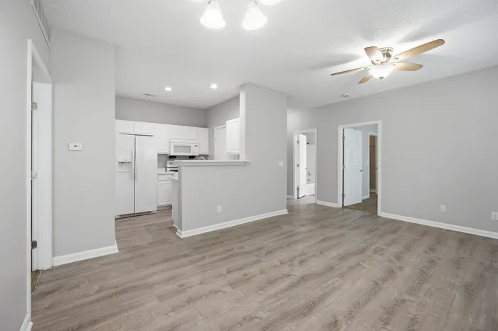 Chic modern apartment with an open-concept living area, featuring stylish hardwood floors, white cabinetry, and ceiling fan for added comfort.