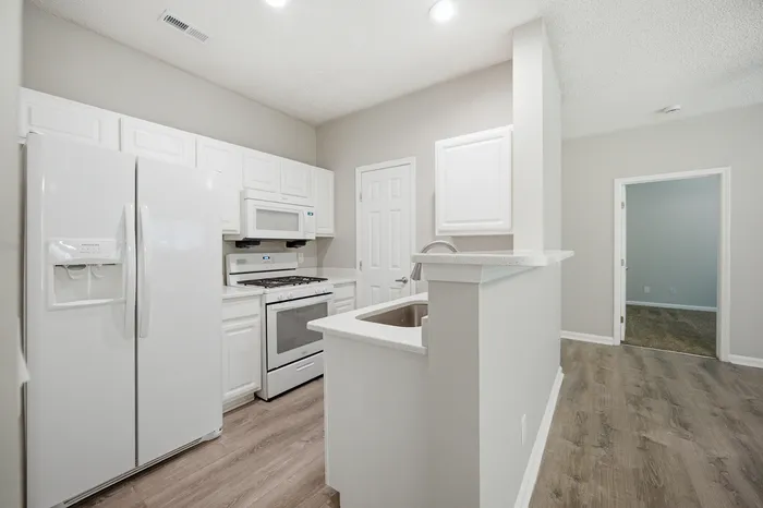 Modern kitchen with sleek white cabinetry, integrated appliances, and elegant hardwood flooring.