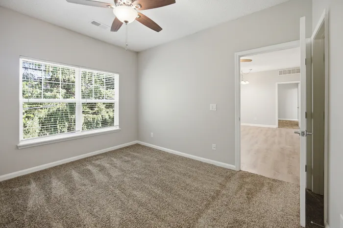 Bright, cozy room with plush carpeting, large window with scenic views, and a ceiling fan for comfort.