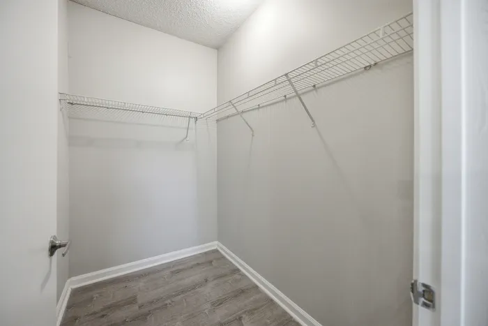 Spacious walk-in closet with clean white wire shelving and modern wood flooring, perfect for organized storage.