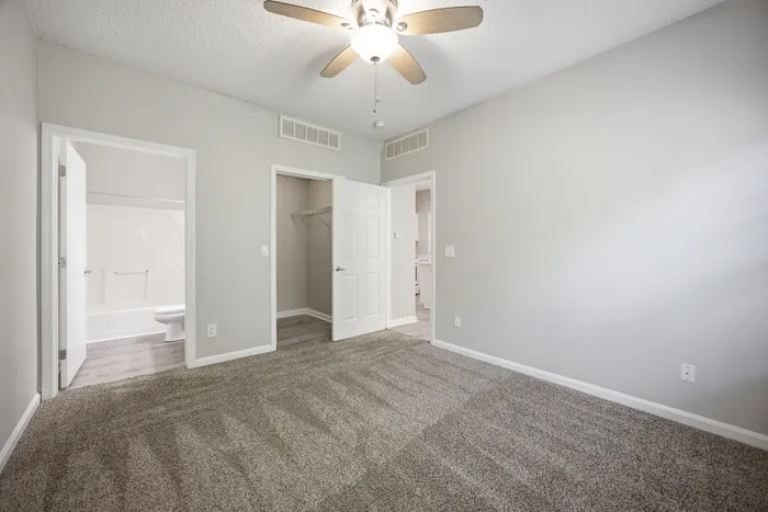Bright and inviting bedroom with plush carpeting, adjacent to a modern bathroom and a spacious walk-in closet.