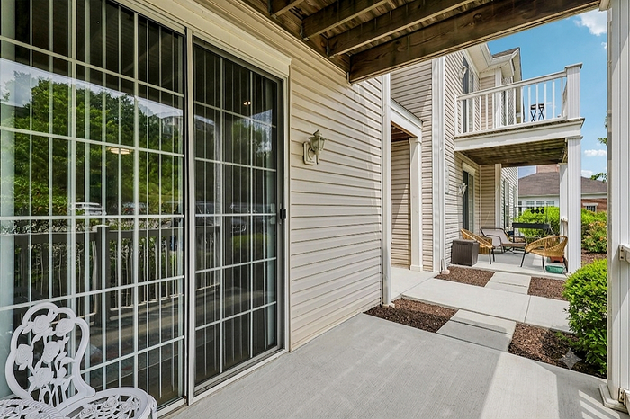 Charming outdoor patio with elegant sliding glass doors, cozy seating area, and inviting greenery, perfect for relaxation and entertaining.