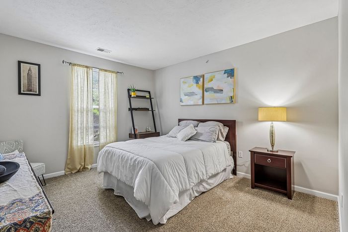 Inviting bedroom with plush carpeting, elegant white bed linens, and stylish contemporary decor, featuring soft natural light and a cozy ambiance.