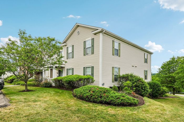 Charming two-story home with classic siding, surrounded by lush greenery and a well-maintained garden, set against a clear blue sky.
