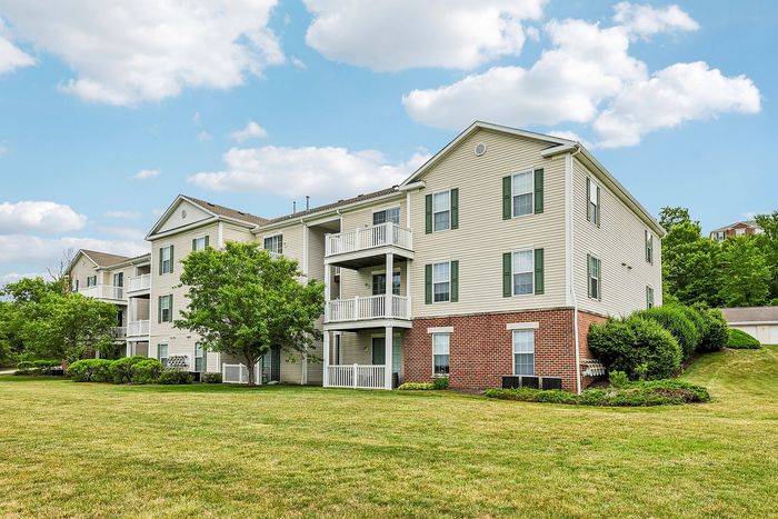 Charming multi-story apartment building surrounded by lush greenery under a bright, clear sky, promising a serene residential living experience.