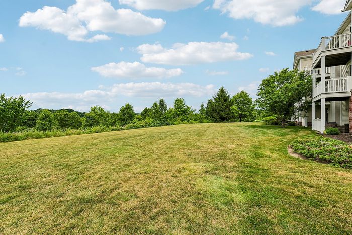 Picturesque apartment view with expansive lush green lawn, mature trees, and inviting balconies under a bright blue sky.