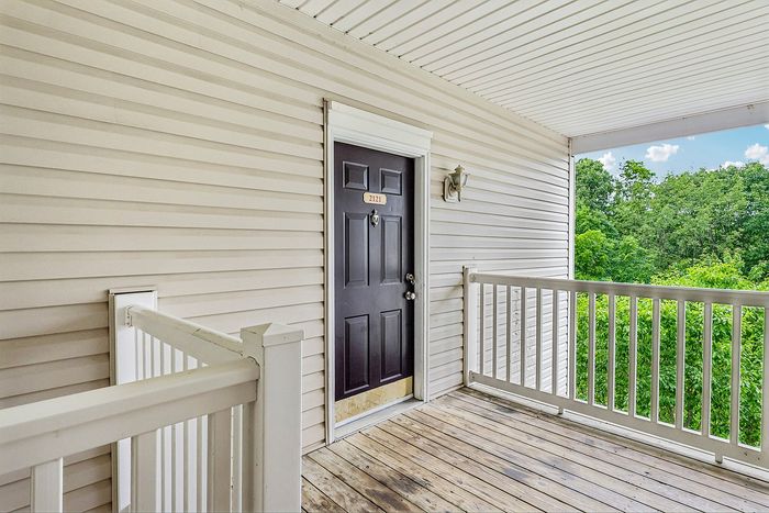 Inviting apartment entrance with elegant black door, located on a charming balcony overlooking lush greenery.
