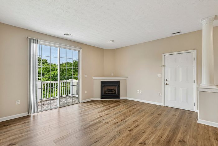 Bright and airy living room with hardwood flooring, a sleek fireplace, and large sliding glass doors opening to a green balcony view.