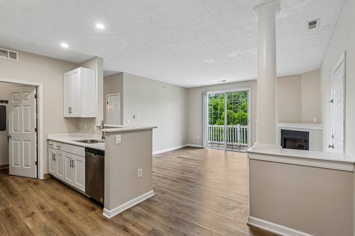 Bright and airy living space with elegant wooden flooring, modern kitchen, and large glass doors opening to a green view.