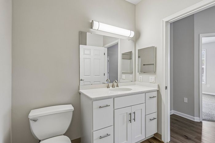 Bright, modern bathroom featuring sleek white cabinetry, elegant countertop, and a large mirror with ambient lighting.