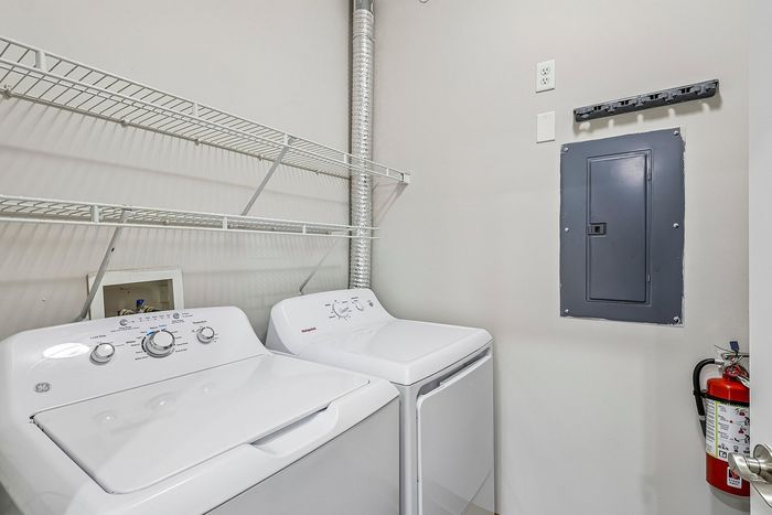 Contemporary laundry room with sleek white washer and dryer, featuring ample storage space and convenient wall-mounted shelving.