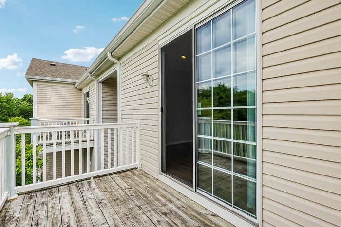 Charming outdoor patio with a wooden deck and elegant sliding glass door, offering a serene view of lush greenery.
