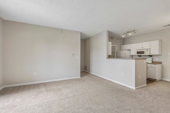 Inviting open-concept apartment with cozy carpeted living space, elegant light fixtures, and modern kitchen featuring bright cabinetry and spacious countertops.