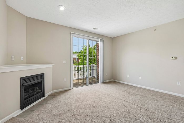 Bright and inviting living room with a cozy fireplace, plush carpeting, and large glass doors leading to a charming balcony.