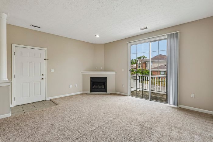 Bright and spacious living room with plush carpet, a cozy fireplace, and large sliding glass doors leading to a serene balcony view.
